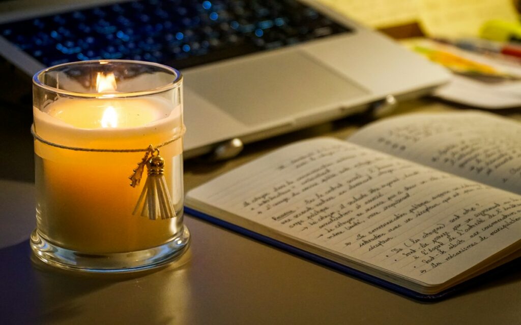 Open handwritten notebook beside a candle and laptop on a table at night